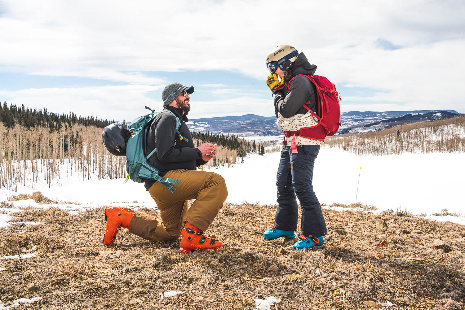 A man proposes on one knee on a Colorado mountaintop during winter.