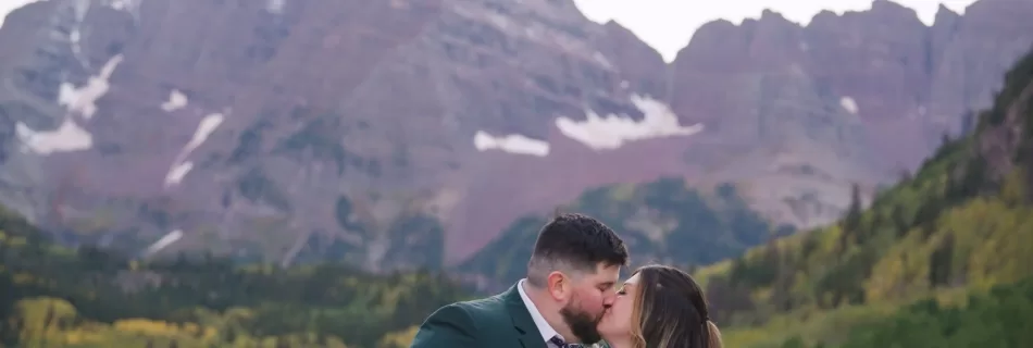 A man and woman in wedding clothes kiss below the Maroon Bells mountains in Colorado